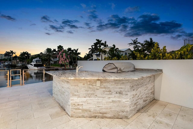 patio terrace at dusk featuring a water view and exterior bar