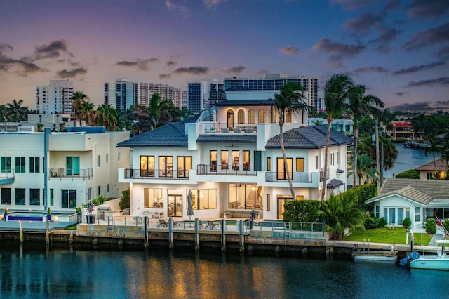 back house at dusk with a water view and a balcony