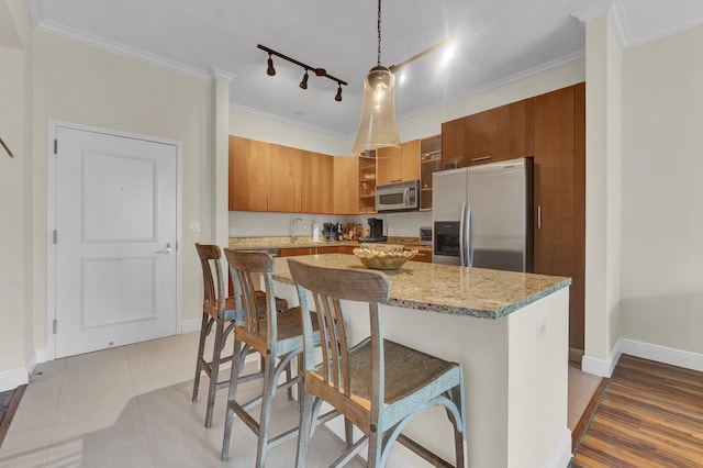 kitchen featuring crown molding, hanging light fixtures, appliances with stainless steel finishes, light stone counters, and a kitchen bar