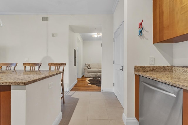 kitchen featuring light stone countertops, dishwasher, a kitchen breakfast bar, ornamental molding, and light tile patterned floors