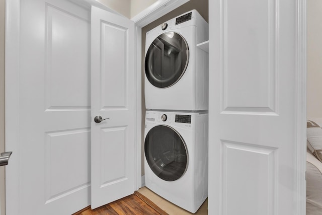 clothes washing area with hardwood / wood-style floors and stacked washer and dryer