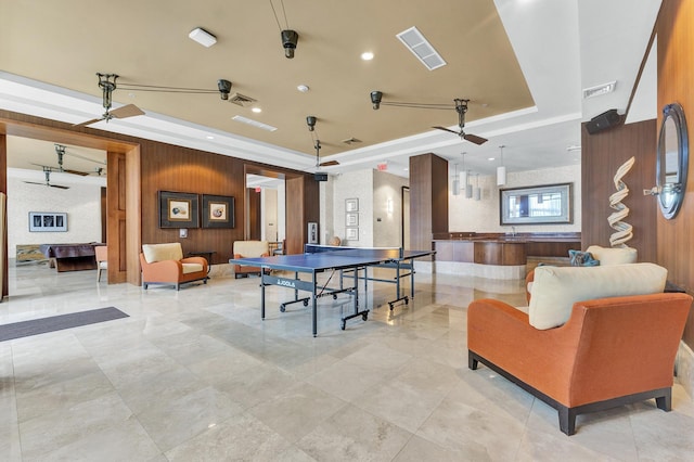 recreation room featuring wood walls, ceiling fan, and a raised ceiling