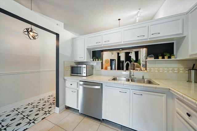 kitchen featuring tile countertops, white cabinetry, stainless steel appliances, decorative light fixtures, and sink