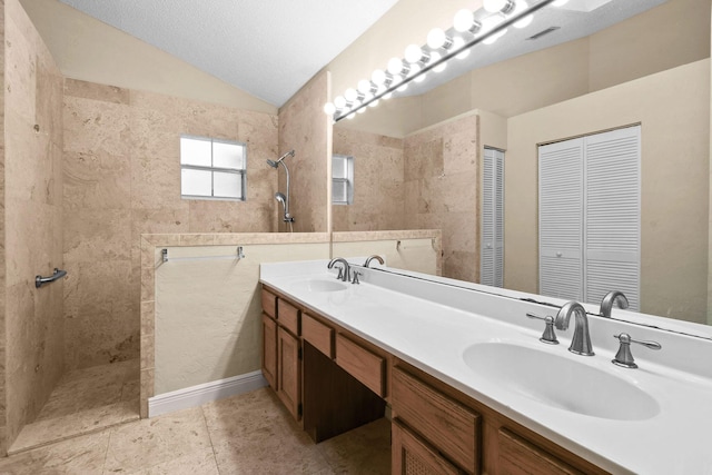 bathroom with lofted ceiling, tile patterned flooring, vanity, tiled shower, and a textured ceiling