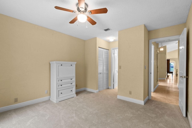 unfurnished bedroom with ceiling fan, light colored carpet, a closet, and a textured ceiling