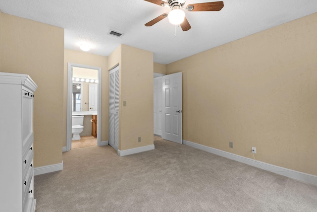 unfurnished bedroom with ensuite bath, light colored carpet, a textured ceiling, a closet, and ceiling fan