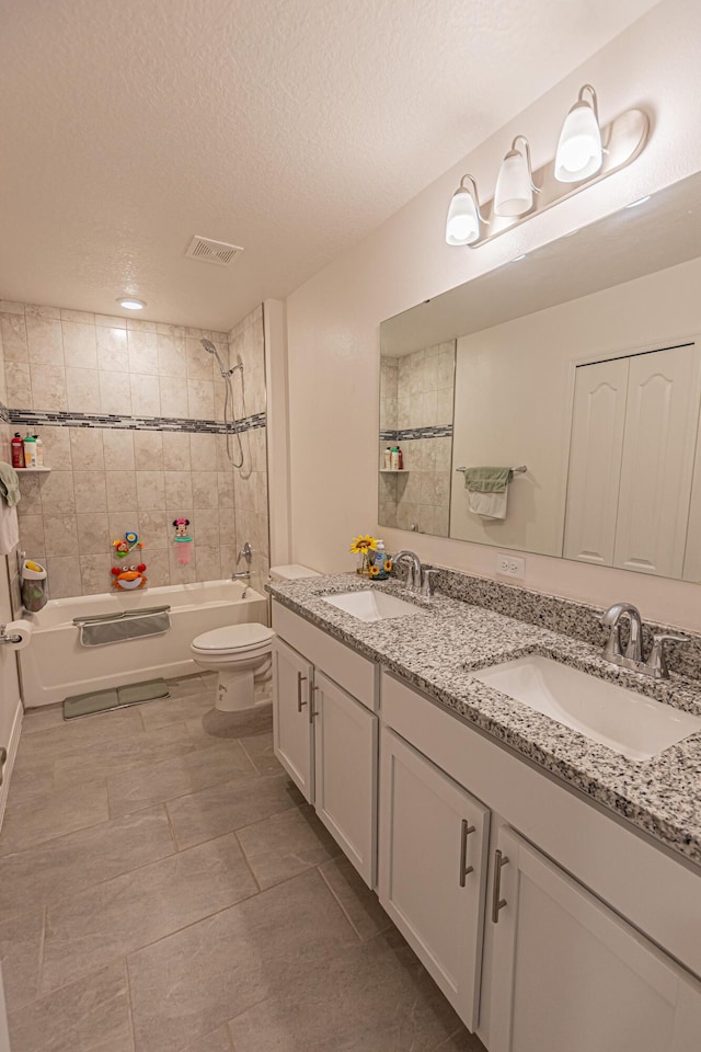 full bathroom with tile patterned floors, toilet, a textured ceiling, vanity, and tiled shower / bath combo