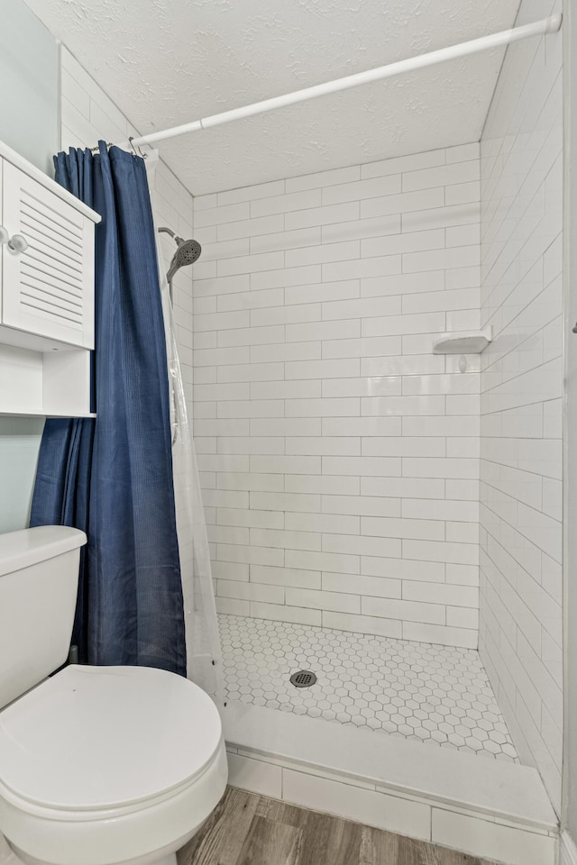 bathroom with a shower with curtain, wood-type flooring, a textured ceiling, and toilet