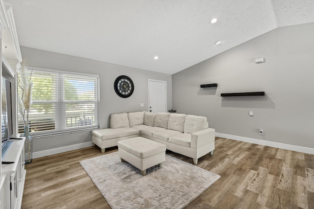 living room featuring lofted ceiling, light hardwood / wood-style floors, and a textured ceiling