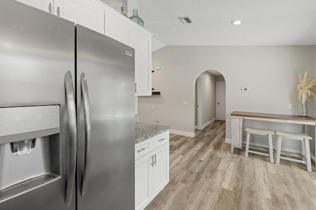 kitchen featuring white cabinetry, stainless steel refrigerator with ice dispenser, light stone countertops, and vaulted ceiling