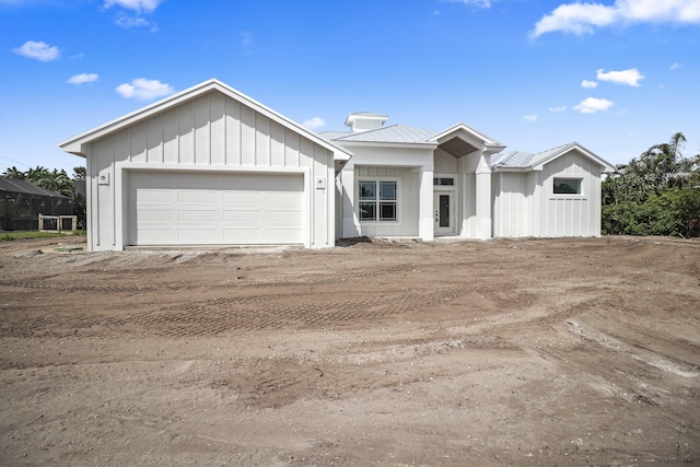 view of front facade with board and batten siding, metal roof, driveway, and a garage