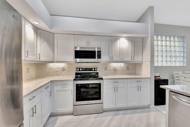 kitchen featuring light stone countertops, light wood finished floors, white cabinets, appliances with stainless steel finishes, and tasteful backsplash