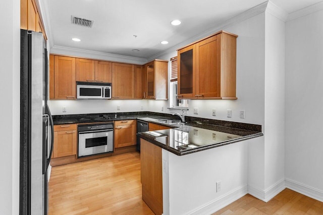 kitchen featuring sink, light wood-type flooring, dark stone countertops, kitchen peninsula, and stainless steel appliances