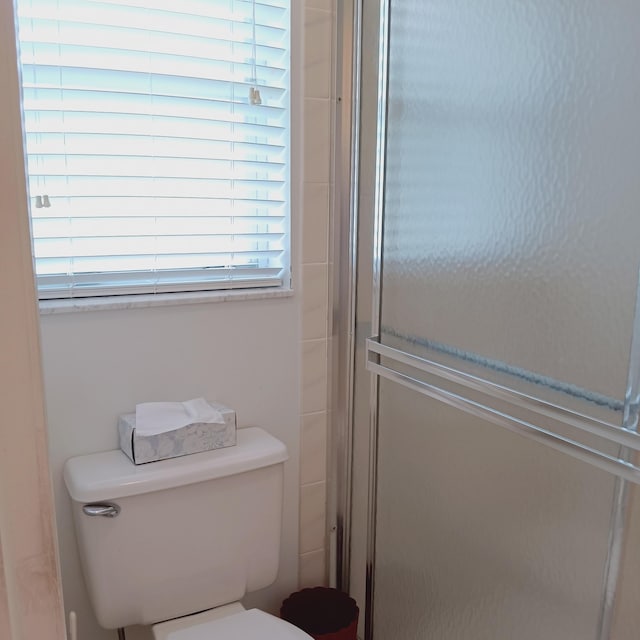 bathroom featuring toilet and a shower with shower door