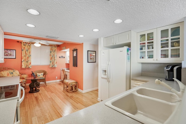 kitchen featuring sink, white appliances, light hardwood / wood-style flooring, white cabinetry, and a textured ceiling