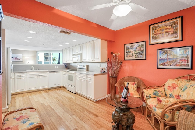 kitchen with white cabinetry, white appliances, a textured ceiling, and light wood-type flooring