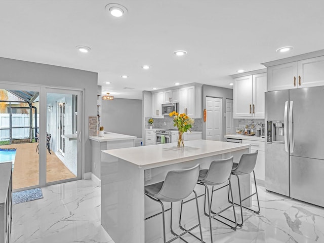 kitchen featuring white cabinets, appliances with stainless steel finishes, a kitchen island, decorative backsplash, and a breakfast bar area