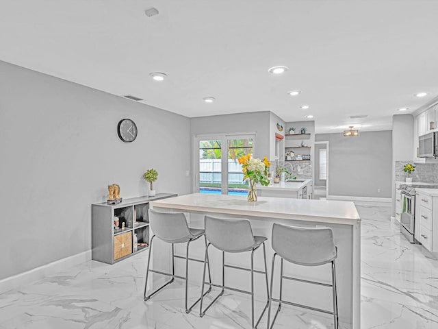 kitchen with a kitchen island, a breakfast bar, decorative backsplash, white cabinetry, and stainless steel electric range oven