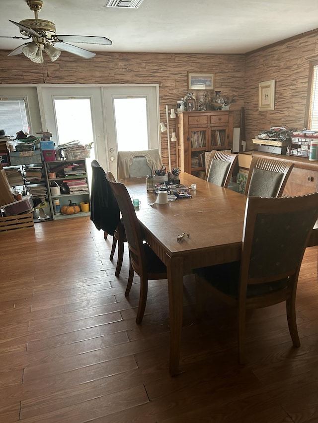 dining space with ceiling fan, french doors, wood walls, and hardwood / wood-style floors