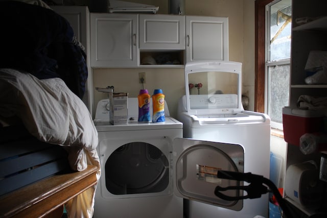 clothes washing area featuring plenty of natural light, washing machine and clothes dryer, and cabinets