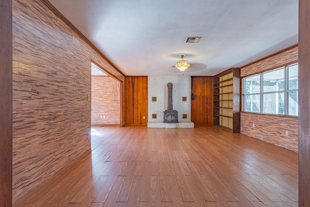 unfurnished living room with hardwood / wood-style flooring, ornamental molding, and a wood stove