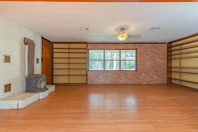 unfurnished living room featuring brick wall, a wood stove, light hardwood / wood-style floors, and built in features