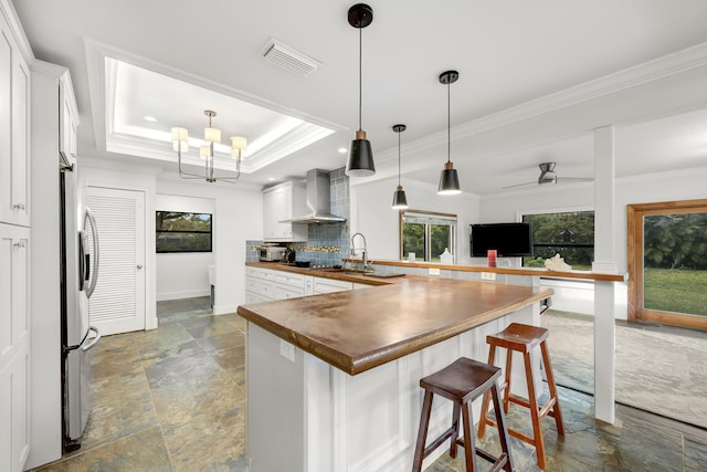 kitchen featuring white cabinetry, ornamental molding, a raised ceiling, and wall chimney exhaust hood