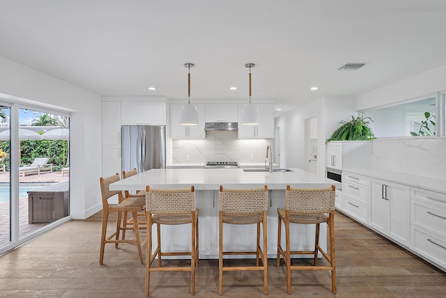 kitchen with decorative light fixtures, backsplash, a center island with sink, and sink