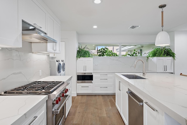 kitchen with separate washer and dryer, appliances with stainless steel finishes, decorative light fixtures, sink, and light stone counters