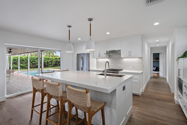 kitchen with an island with sink, appliances with stainless steel finishes, pendant lighting, white cabinets, and sink