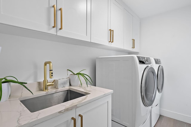 washroom featuring cabinets, sink, washer and clothes dryer, and light hardwood / wood-style floors