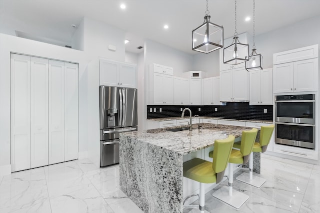 kitchen with sink, hanging light fixtures, stainless steel appliances, a kitchen island with sink, and white cabinets