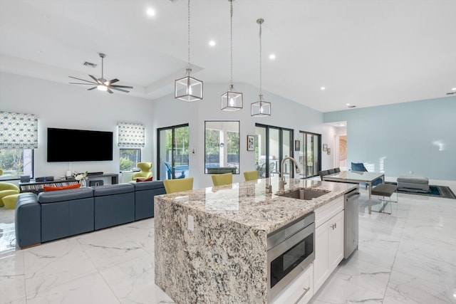 kitchen with appliances with stainless steel finishes, white cabinetry, sink, a kitchen island with sink, and light stone counters