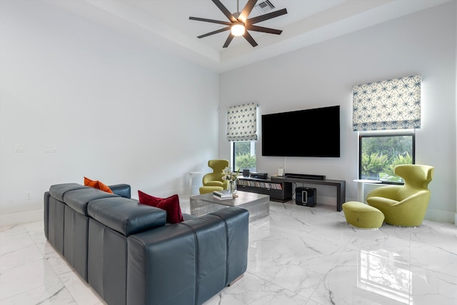 living room with a raised ceiling, ceiling fan, and a high ceiling