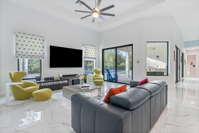 living room featuring a raised ceiling, a high ceiling, and ceiling fan