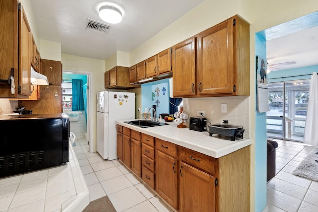 kitchen with a wealth of natural light, tile countertops, sink, and white refrigerator