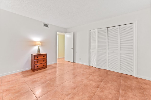 unfurnished bedroom featuring a textured ceiling, a closet, and light tile patterned floors