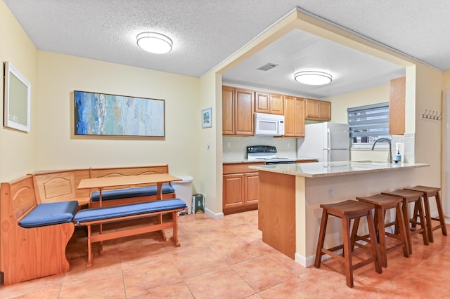 kitchen with white appliances, decorative backsplash, sink, a kitchen breakfast bar, and kitchen peninsula