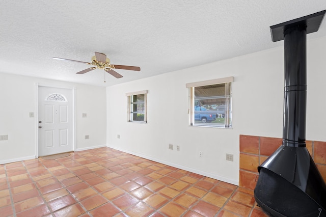 living room featuring ceiling fan, a wood stove, a textured ceiling, and light tile patterned floors