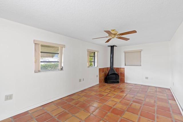 unfurnished living room with a textured ceiling, ceiling fan, tile patterned floors, and a wood stove