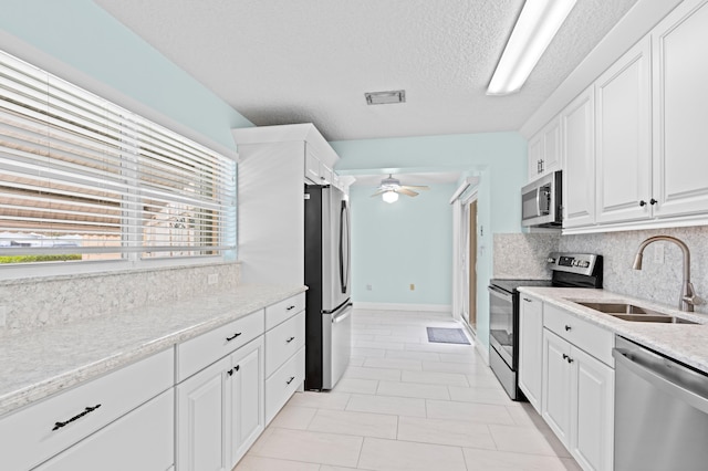 kitchen featuring appliances with stainless steel finishes, white cabinetry, sink, backsplash, and ceiling fan