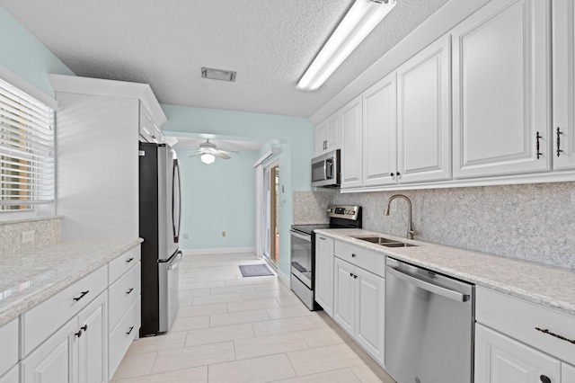 kitchen with a textured ceiling, white cabinetry, stainless steel appliances, sink, and ceiling fan