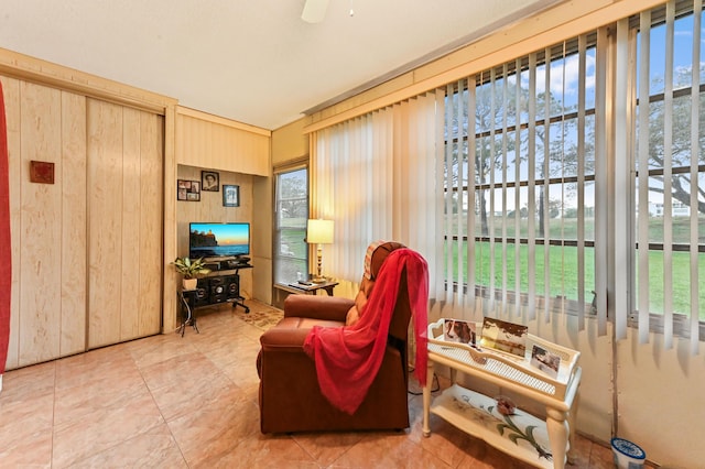 sitting room with ceiling fan, a wealth of natural light, wooden walls, and tile patterned flooring