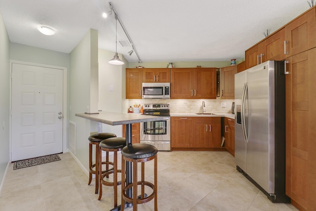 kitchen featuring rail lighting, appliances with stainless steel finishes, pendant lighting, a breakfast bar, and sink