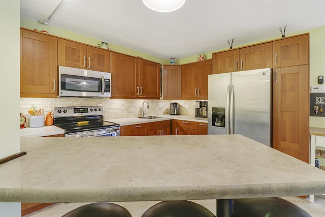 kitchen featuring a kitchen bar, stainless steel appliances, decorative backsplash, sink, and kitchen peninsula