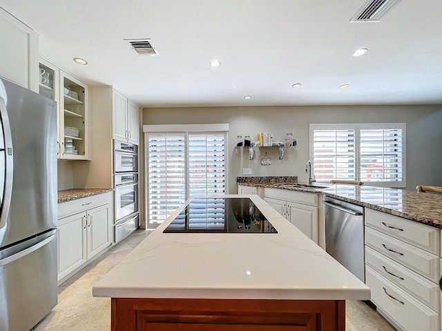 kitchen featuring sink, appliances with stainless steel finishes, light stone countertops, white cabinets, and a kitchen island