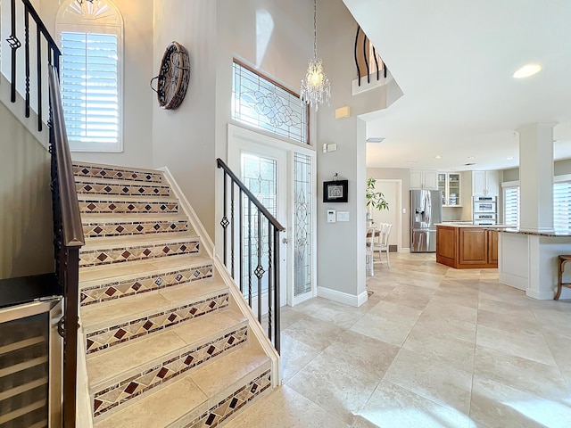 staircase featuring wine cooler, a healthy amount of sunlight, a high ceiling, and a notable chandelier