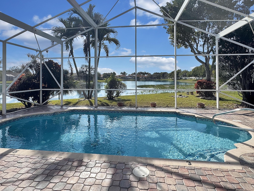 view of pool with a lanai, a water view, a lawn, and a patio area