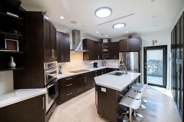 kitchen with appliances with stainless steel finishes, wall chimney range hood, an island with sink, a kitchen breakfast bar, and sink