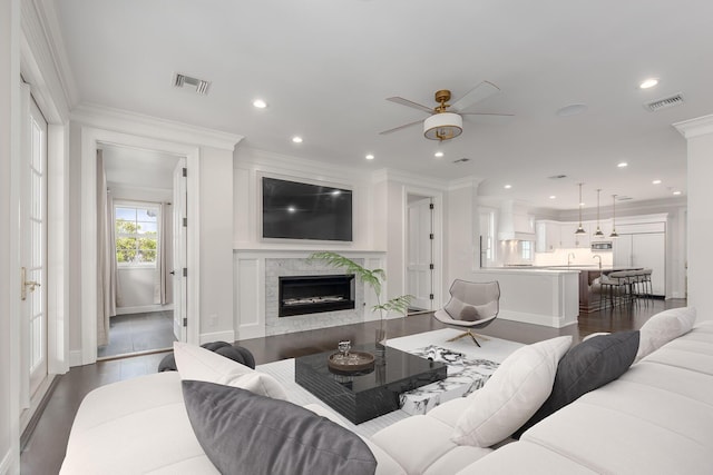 living room with ceiling fan, dark wood-type flooring, a premium fireplace, and crown molding